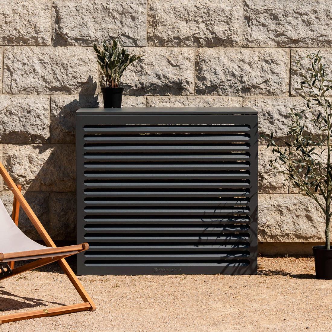 Cache clim gris anthracite (RAL 7016) Cabanaclim – taille L – mise en situation déco extérieure. Finition en aluminium haut de gamme, conçue pour habiller votre clim ou pompe à chaleur avec style. Un choix esthétique et pratique.