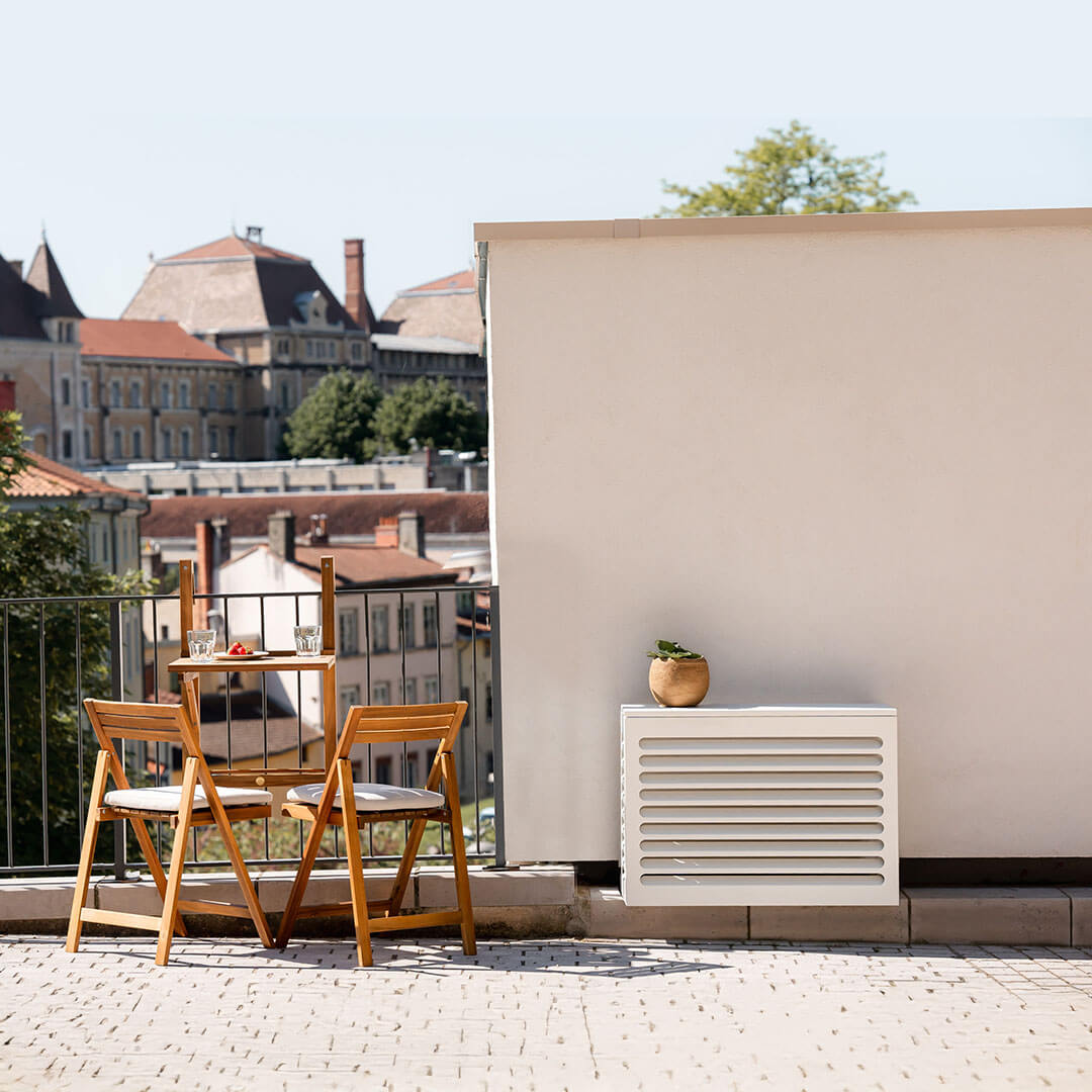 Cache clim Cabanaclim blanc installé sur un balcon urbain avec table en bois et vue sur les toits