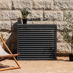 Cache clim gris anthracite (RAL 7016) Cabanaclim – taille L – mise en situation déco extérieure. Finition en aluminium haut de gamme, conçue pour habiller votre clim ou pompe à chaleur avec style. Un choix esthétique et pratique.
