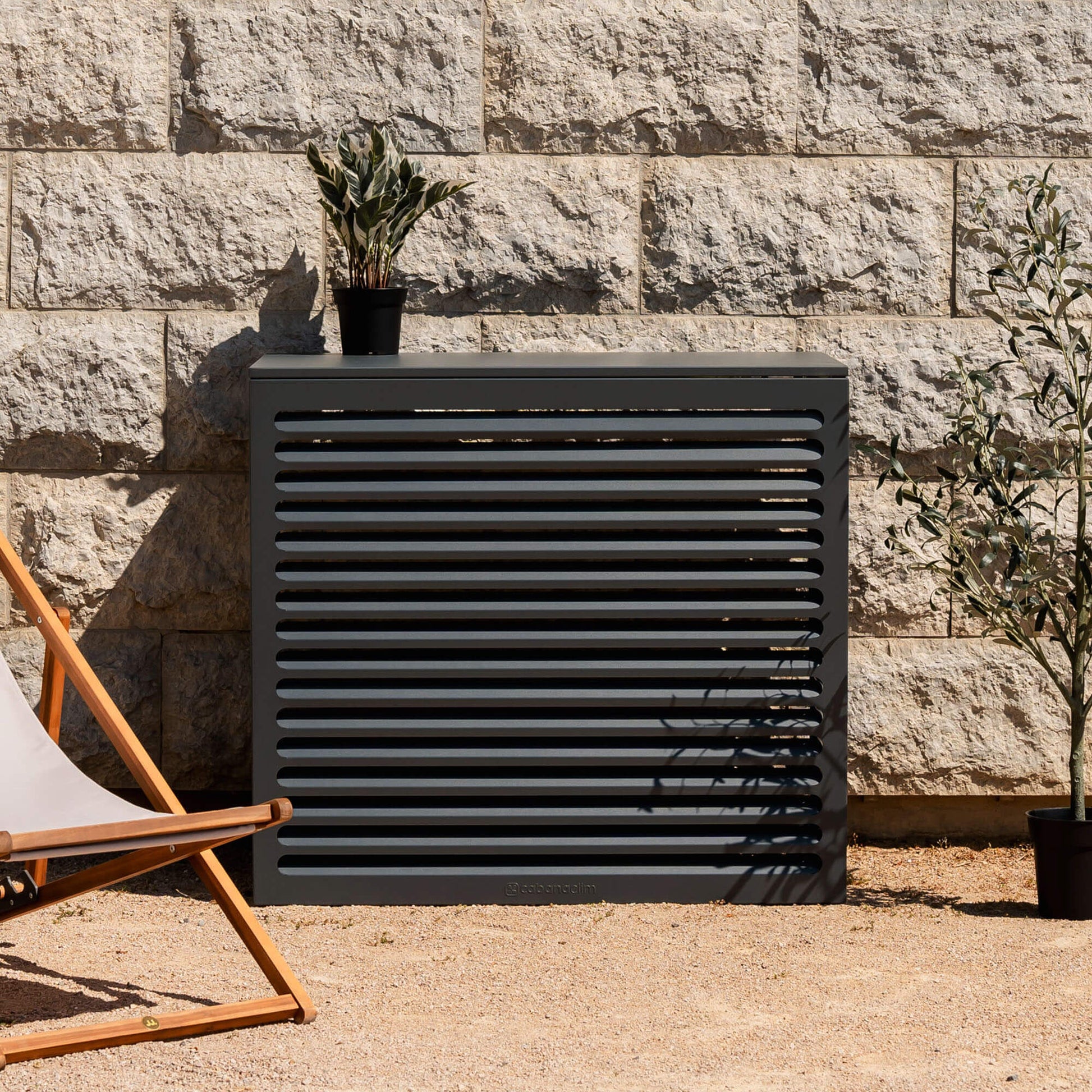 Cache clim gris anthracite (RAL 7016) Cabanaclim – taille L – mise en situation déco extérieure. Finition en aluminium haut de gamme, conçue pour habiller votre clim ou pompe à chaleur avec style. Un choix esthétique et pratique.