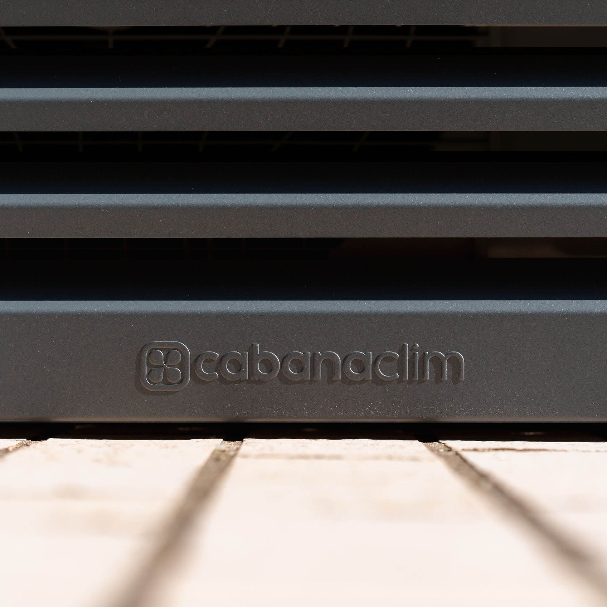 Cache clim gris anthracite (RAL 7016) Cabanaclim – vue du logo embossé face. Structure ventilée et design, idéale pour sublimer une façade ou un jardin. Un rendu soigné qui allie déco et performance.