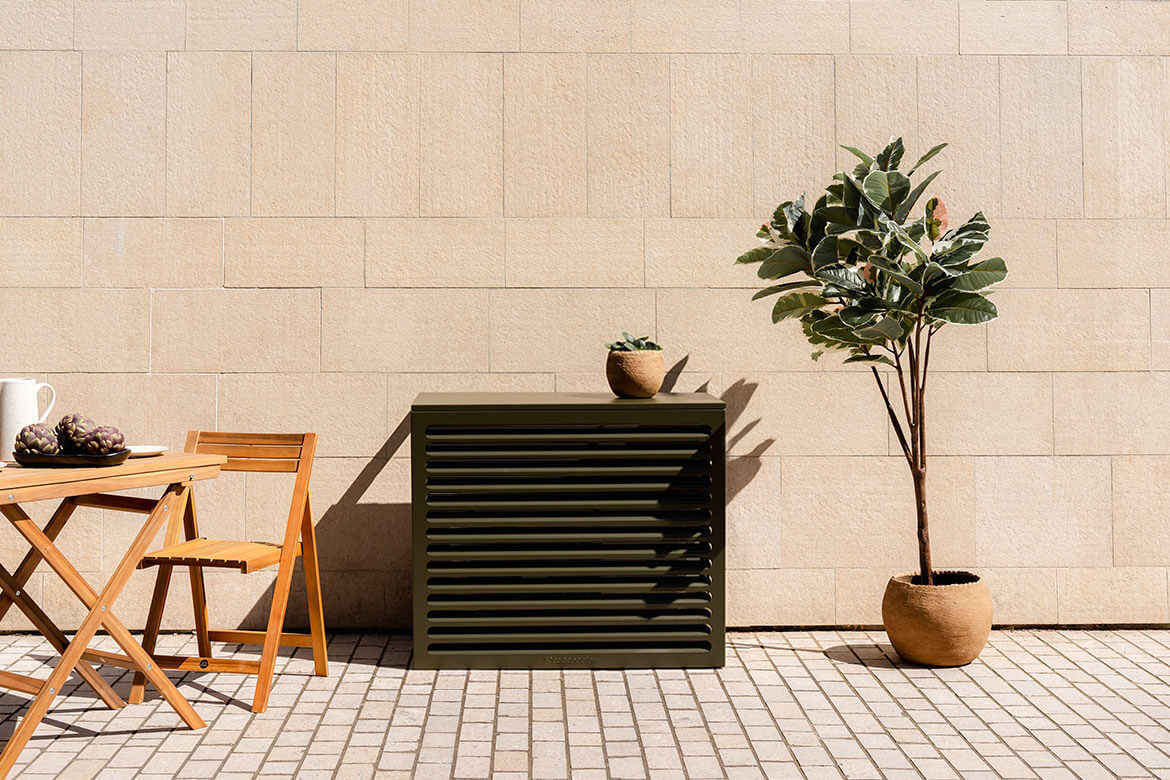 Cache clim kaki Cabanaclim dans un décor méditerranéen avec mobilier bois, mur clair et plante en pot.