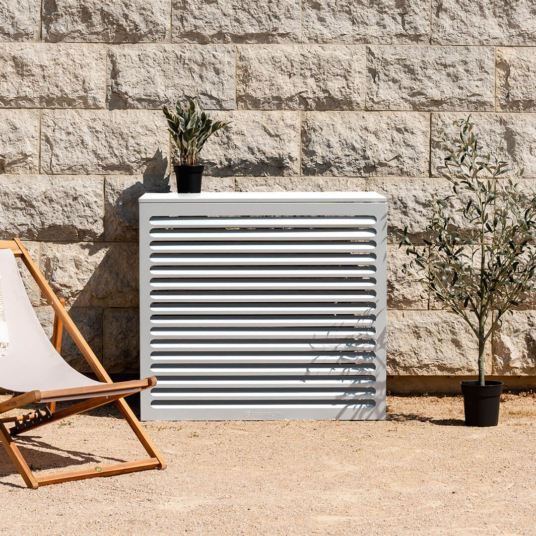 Cache clim blanc (RAL 9010) – taille L, installé avec soin – vue de face avec déco. Structure ventilée et design, idéale pour sublimer une façade ou un jardin. Un rendu soigné qui allie déco et performance.