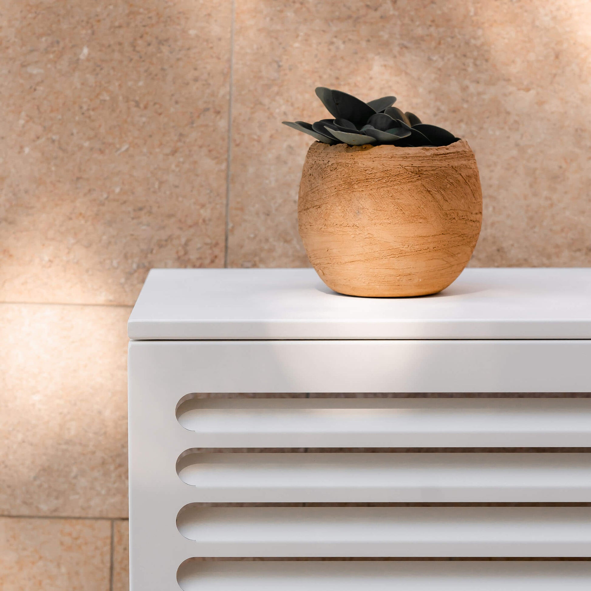 Cache clim blanc (RAL 9010) Cabanaclim – zoom sur le cache en situation réelle avec pot de fleur décoratif posé dessus. Solution esthétique pour climatisation ou pompe à chaleur, intégrée avec goût dans l’espace extérieur.