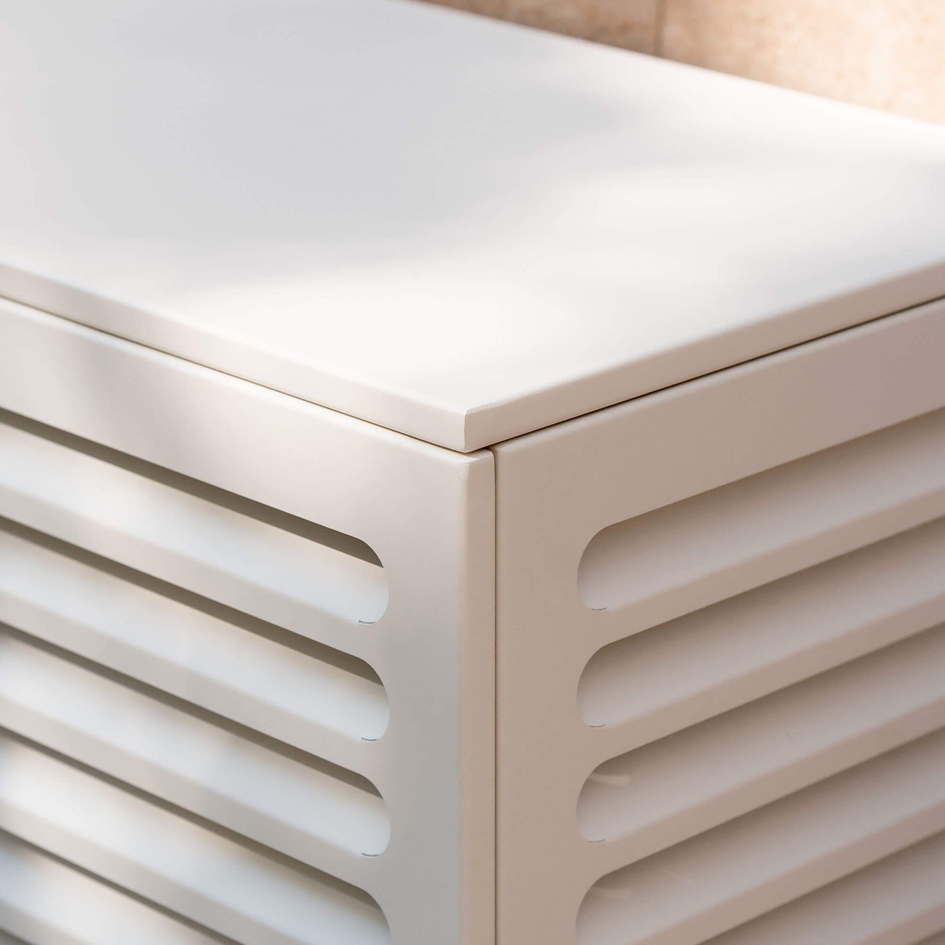 Cache clim blanc crème (RAL 9010) pour climatiseur ou pompe à chaleur – vue d’angle zoomée sur fond de mur clair, aluminium thermolaqué avec persiennes, protection esthétique et durable pour unité extérieur