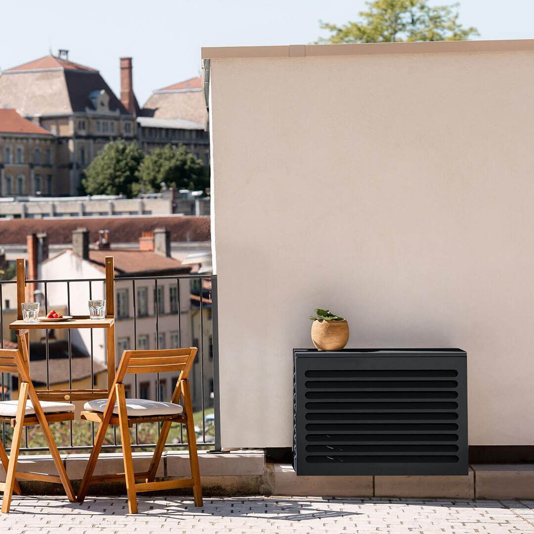 Pose de climatisation autorisée avec un cache clim de taille XS gris anthracite RAL7016 sur un balcon, installé contre un mur blanc, avec une vue urbaine en arrière-plan
