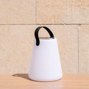 Lampe solaire d’extérieur blanche avec poignée noire, posée sur une table en bois en plein soleil