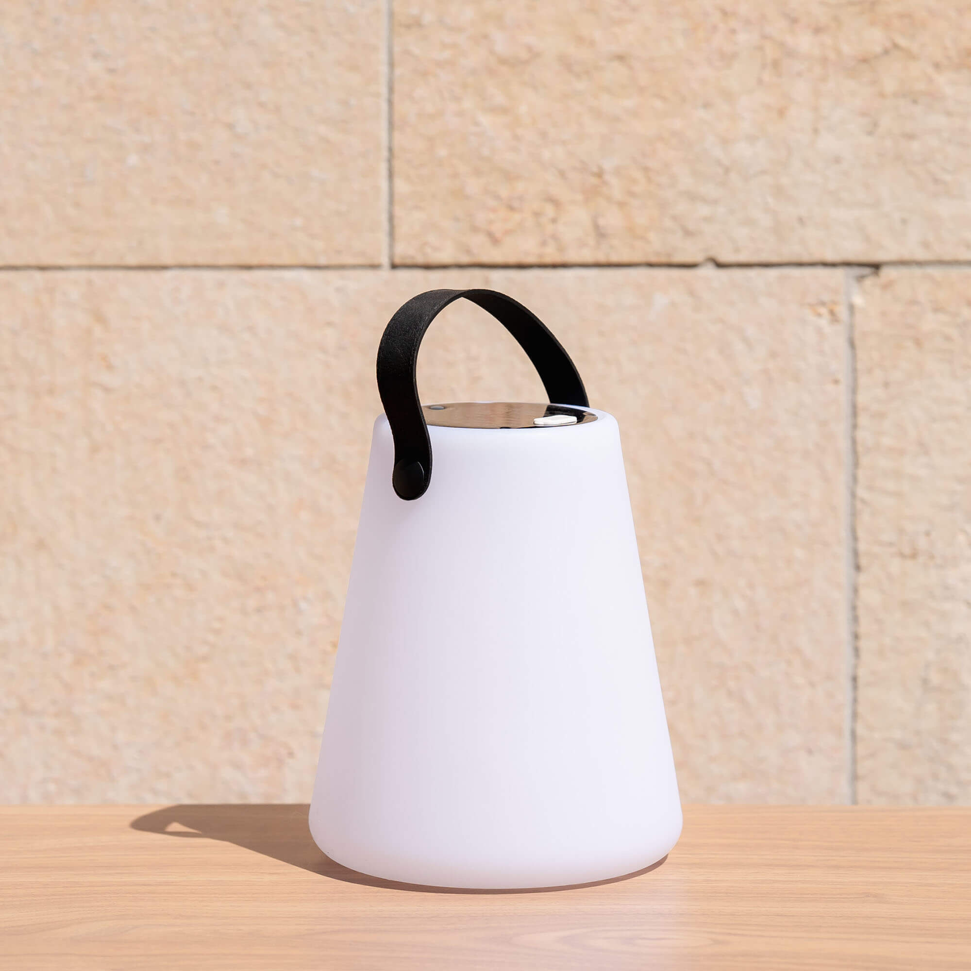 Lampe solaire d’extérieur blanche avec poignée noire, posée sur une table en bois en plein soleil
