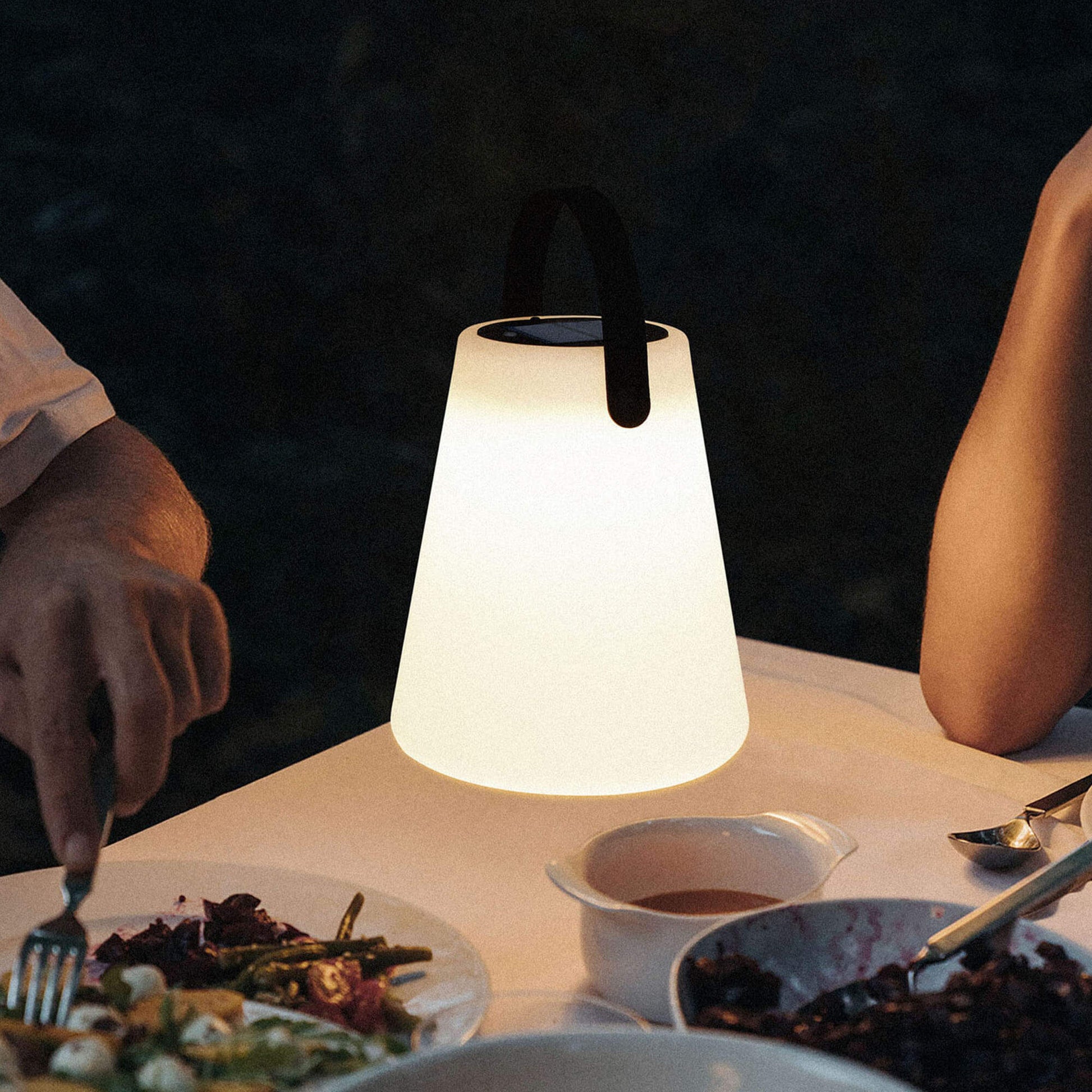 Lampe solaire d’extérieur allumée sur une table de dîner en plein air, créant une ambiance chaleureuse et intime